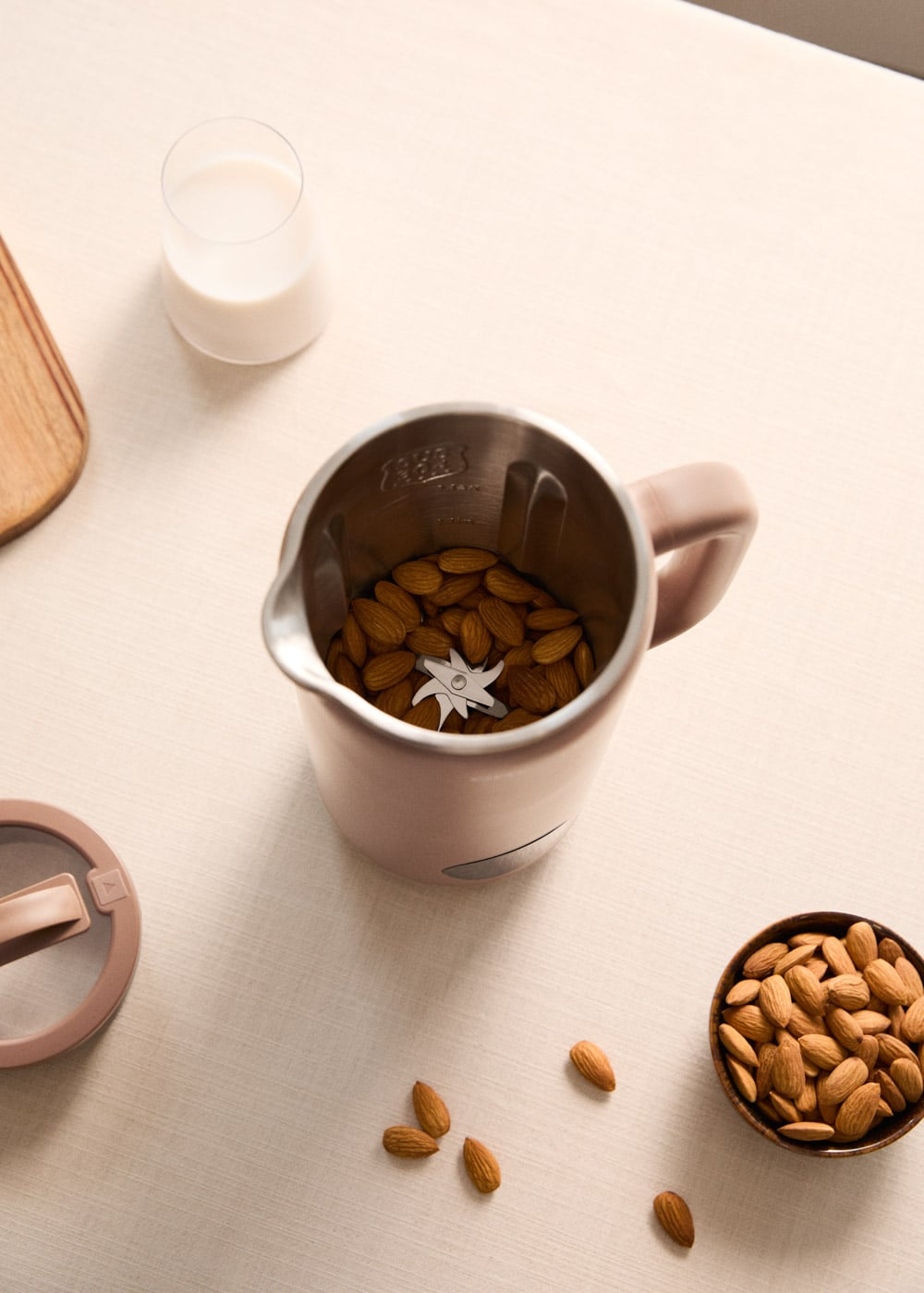 Una batidora con almendras, al lado un cuenco con almendras y un vaso de leche.
