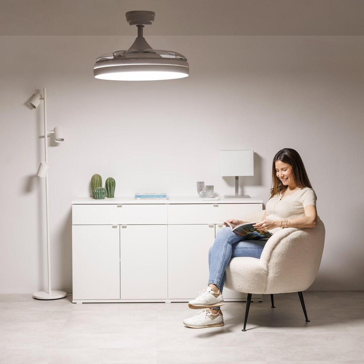 Una donna seduta su una poltrona soffice legge una rivista. Una moderna ventola a soffitto è sopra.