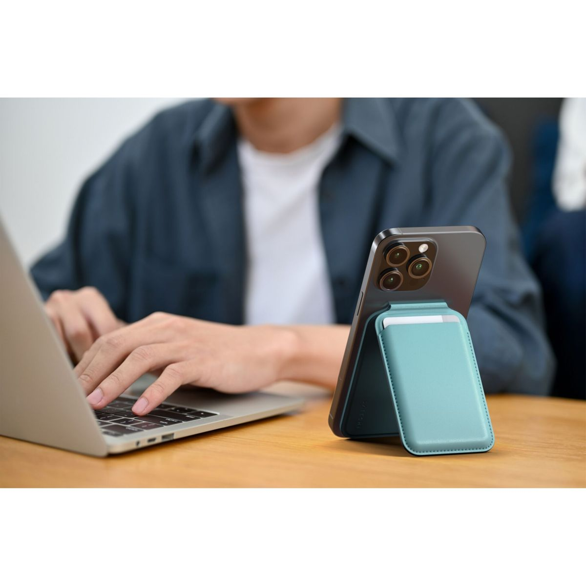 Un uomo digita su un laptop con un telefono e un supporto blu accanto.