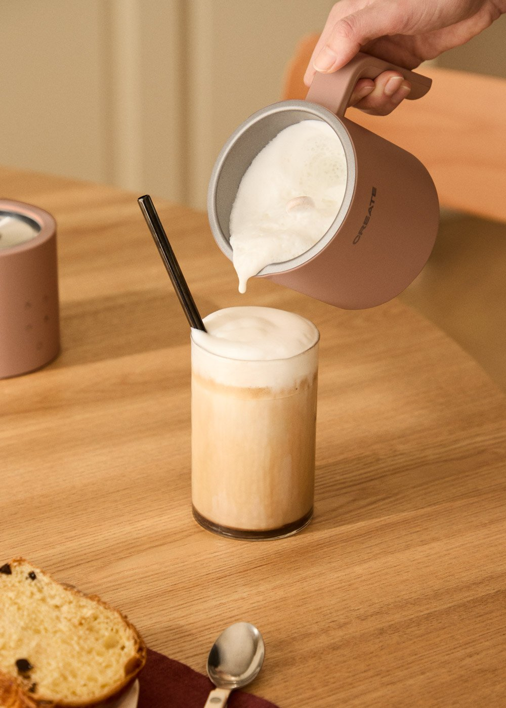 Espuma vertiéndose de una jarra en un vaso de café con leche y pajita.