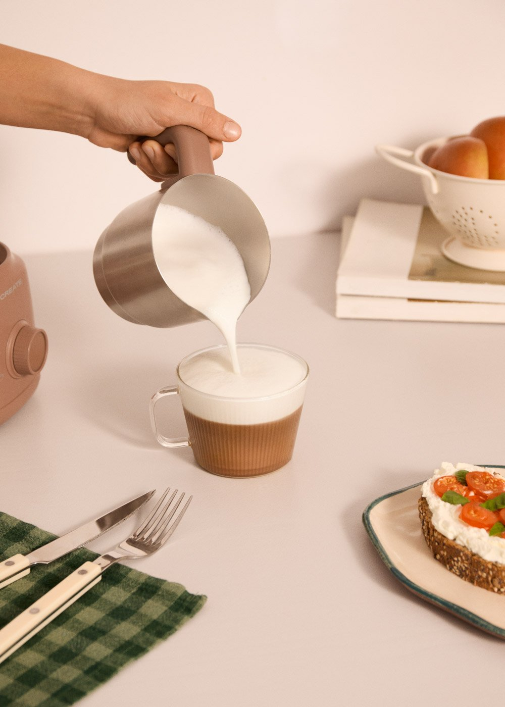 La leche se vierte en una taza de café. Un cuchillo, tenedor y tostada con queso crema están en la mesa.