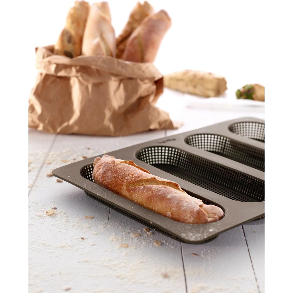 Ein Baguette liegt in einer Backform, weitere im Hintergrund in einer Papiertüte.