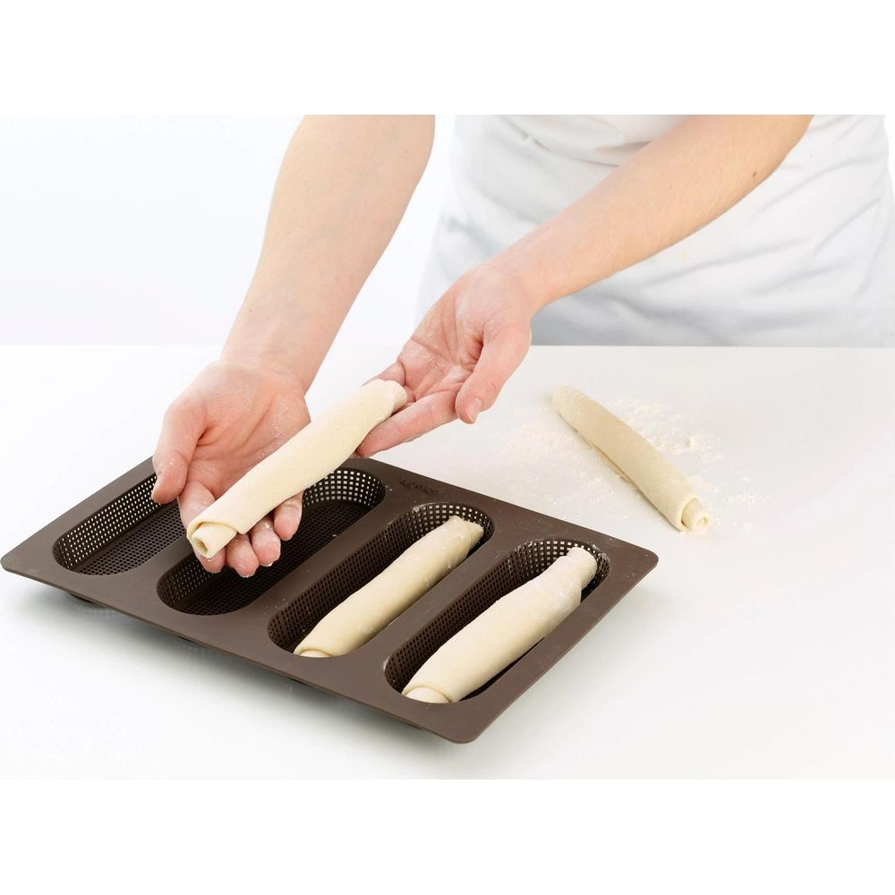 Hände legen Teigrollen in eine braune Backform für Baguettes.