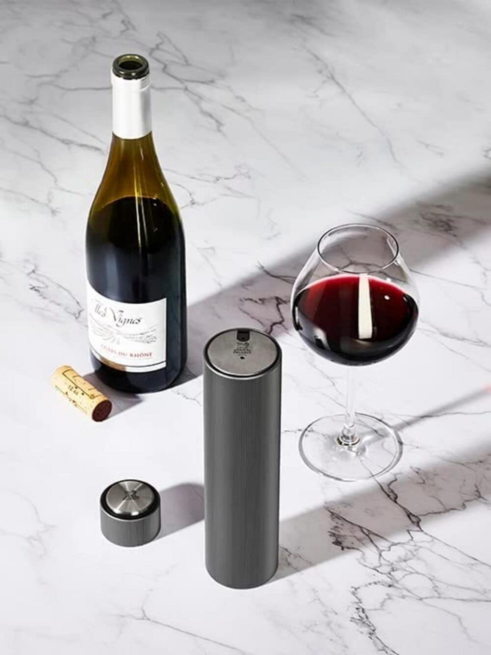 Una bottiglia di vino, un bicchiere di vino rosso, un cavatappi e un tappo su marmo.