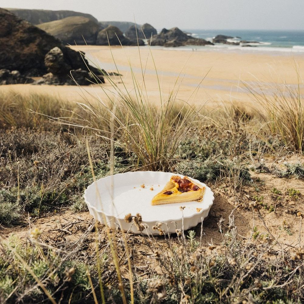 Una fetta di quiche su un piatto sulla spiaggia, con onde sullo sfondo.
