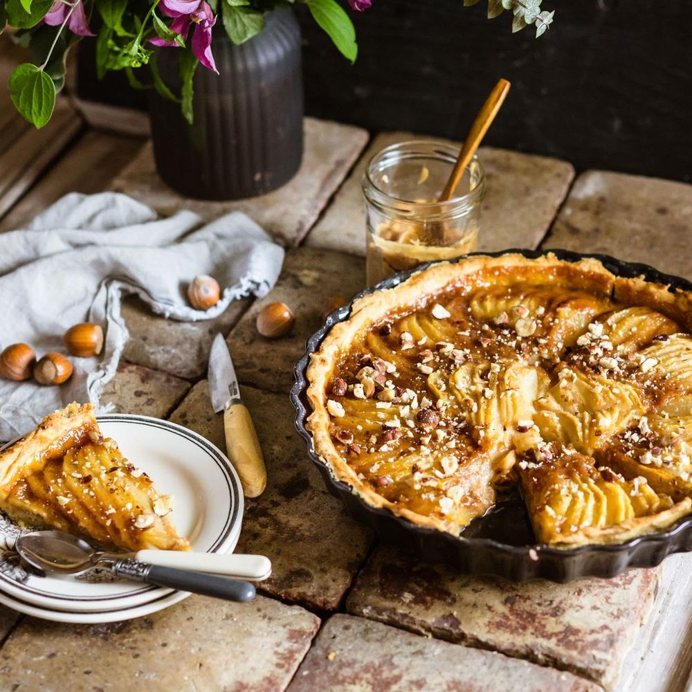 Una torta di mele intera e una fetta con noci e caramello su tavolo rustico.