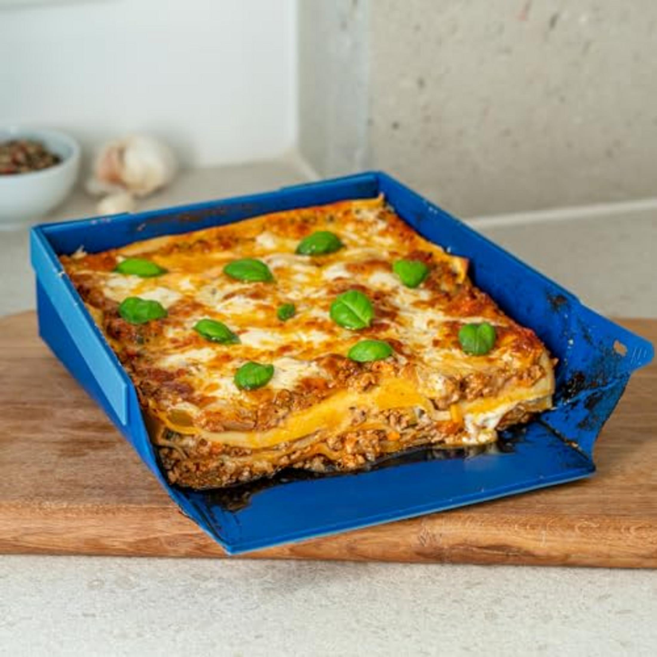 Lasagne in einer blauen Auflaufform, garniert mit Basilikumblättern.