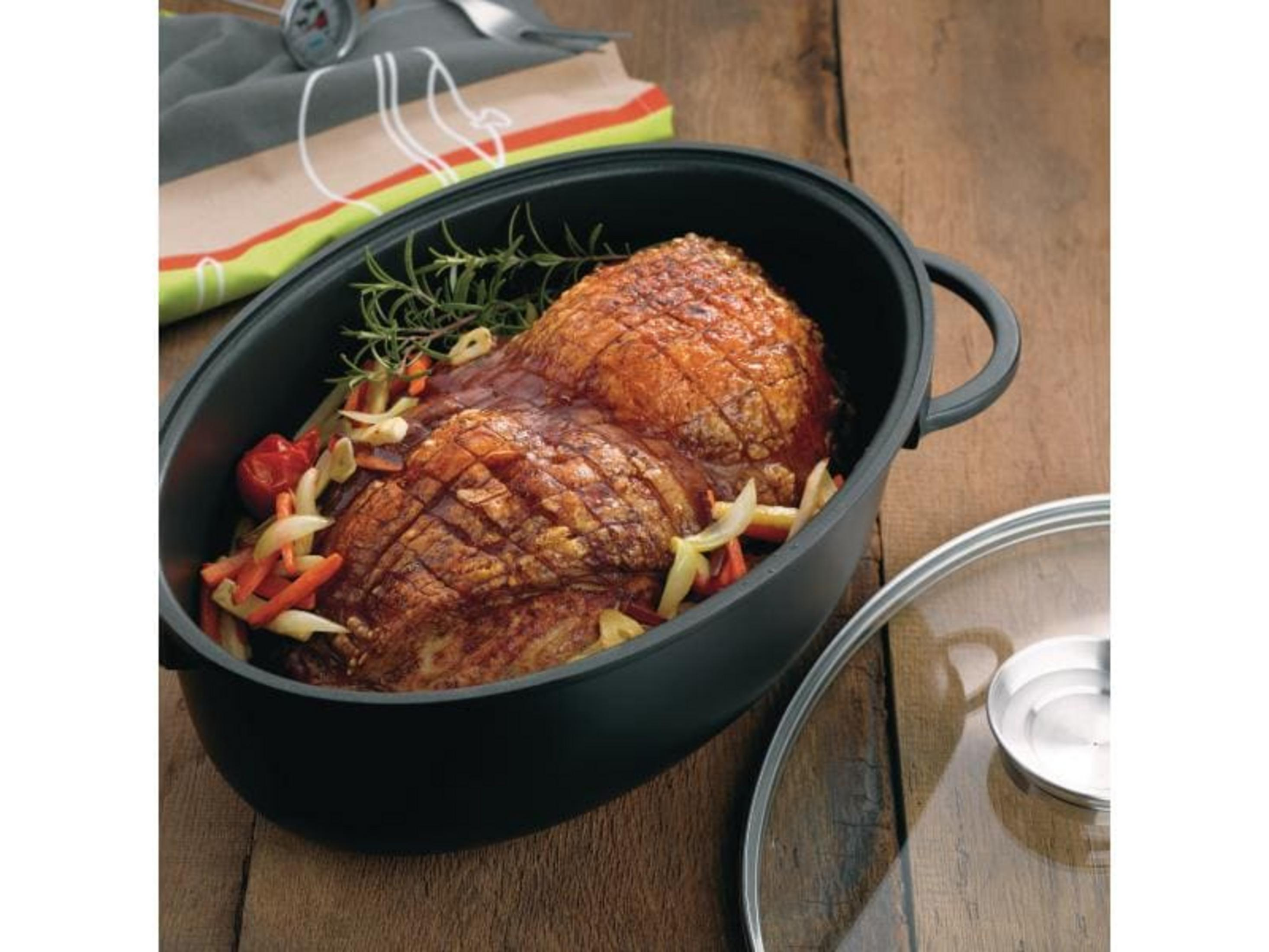 Un morceau de viande rôtie avec des légumes dans une cocotte noire sur table en bois.