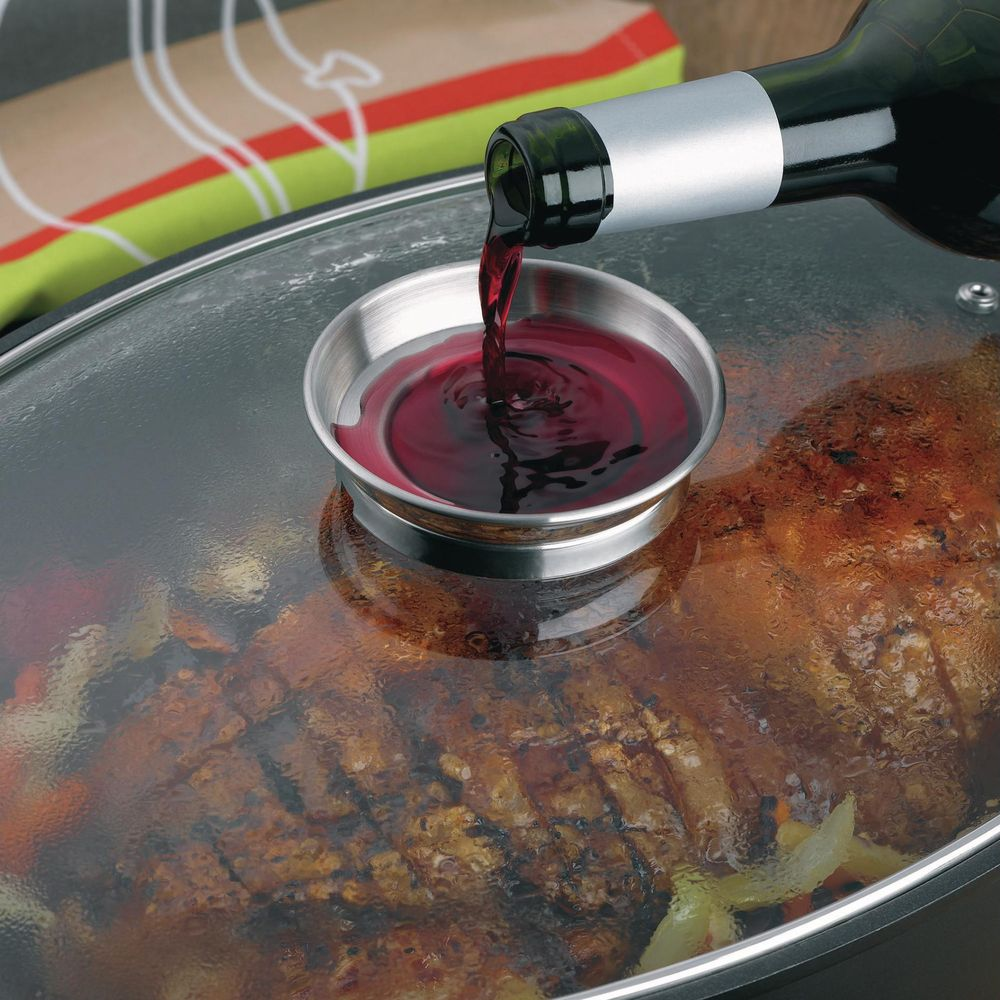 Du vin rouge est versé d'une bouteille dans une petite tasse en métal sur un couvercle en verre sur de la nourriture.
