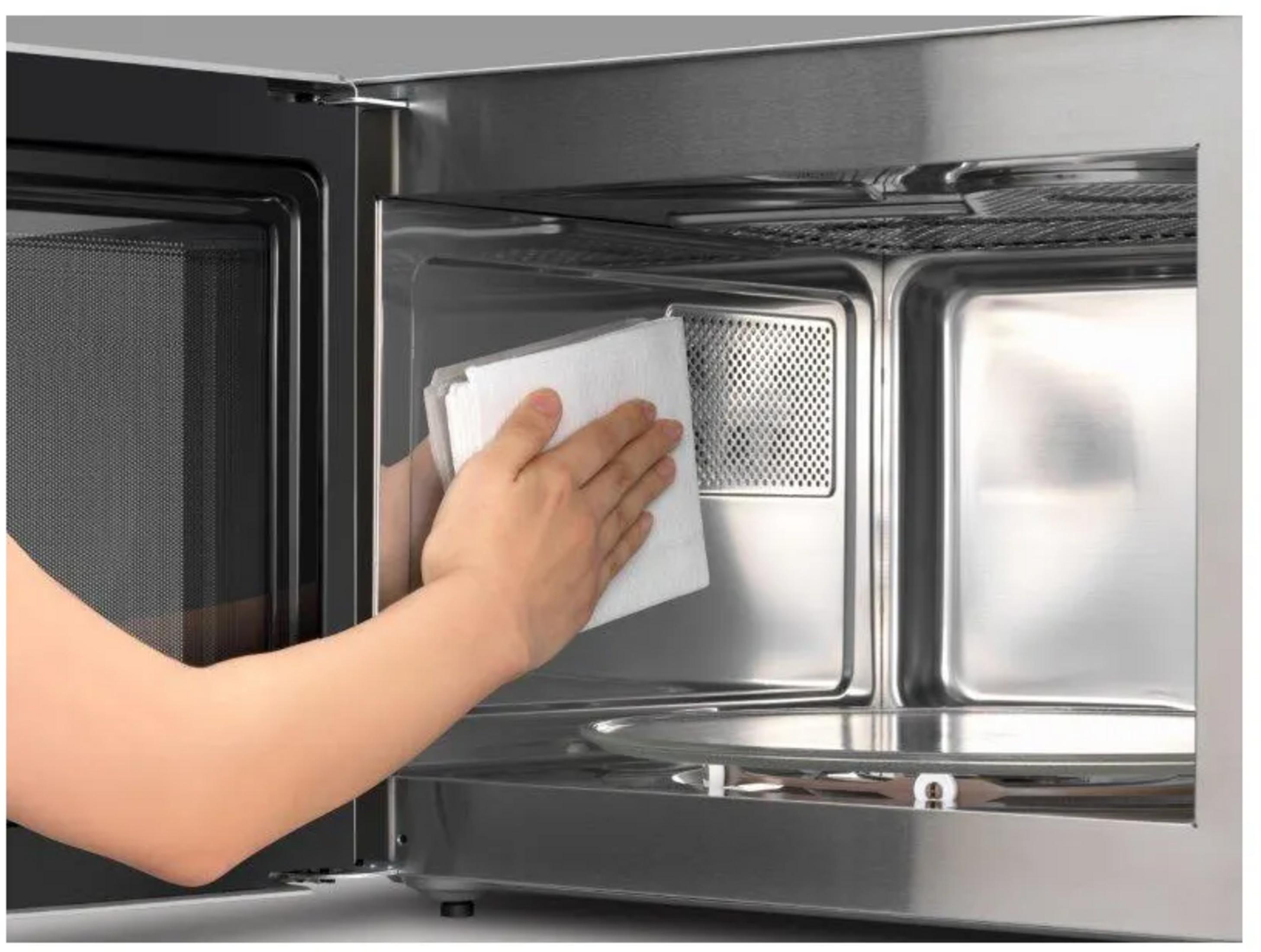 Une main nettoie l'intérieur d'un micro-ondes avec un chiffon blanc.