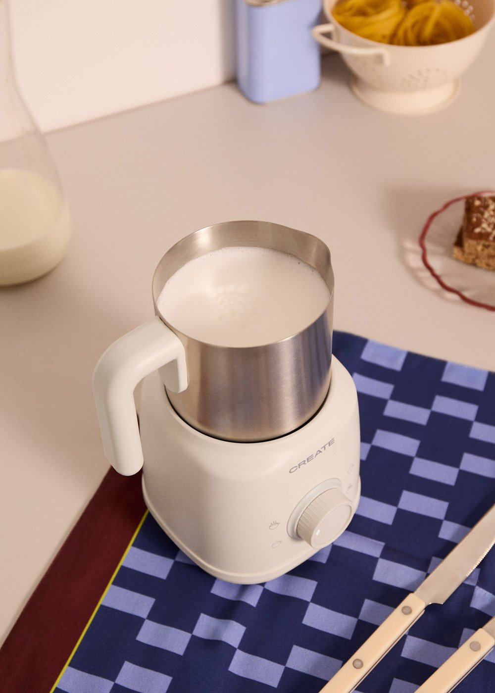 Un espumador de leche blanco con leche está sobre un paño a cuadros.
