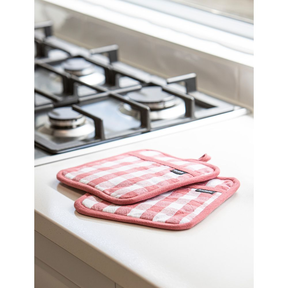 Deux maniques à carreaux rouges et blancs sur un comptoir à côté d'une cuisinière à gaz.