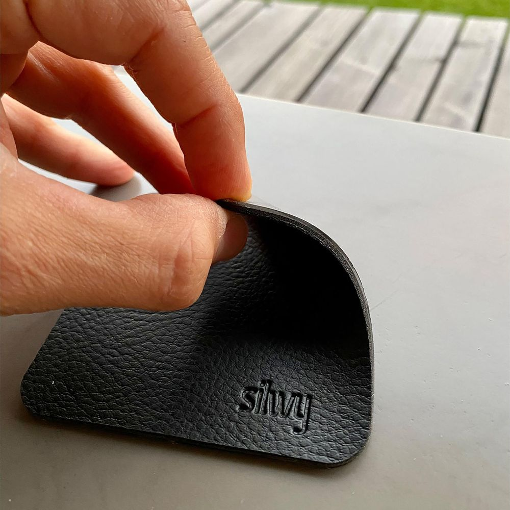 Une main décolle un patch en cuir noir texturé avec le mot 'silvy' en relief.