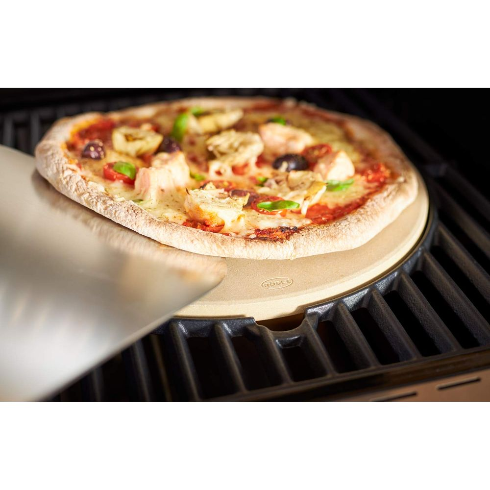 Una pizza viene fatta scivolare su una pietra per pizza su una griglia con una pala per pizza.