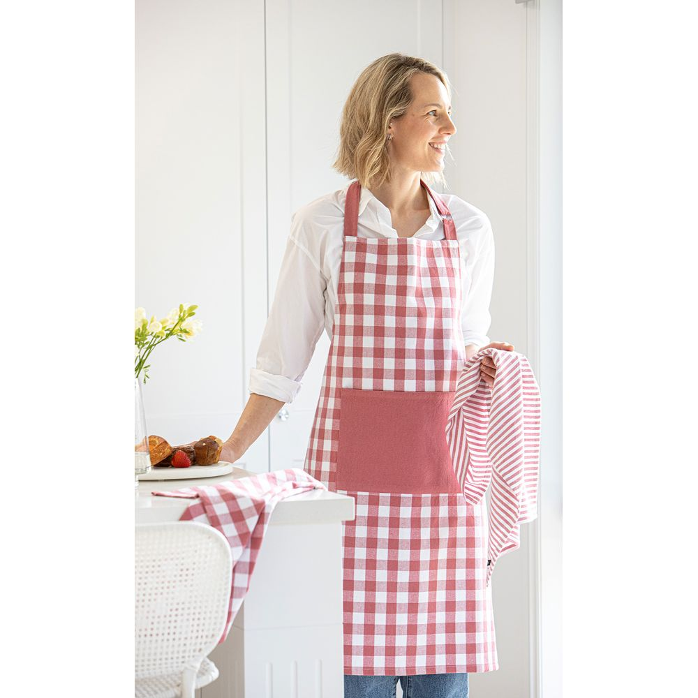 Femme en tablier à carreaux tenant une serviette ; muffins sur table.