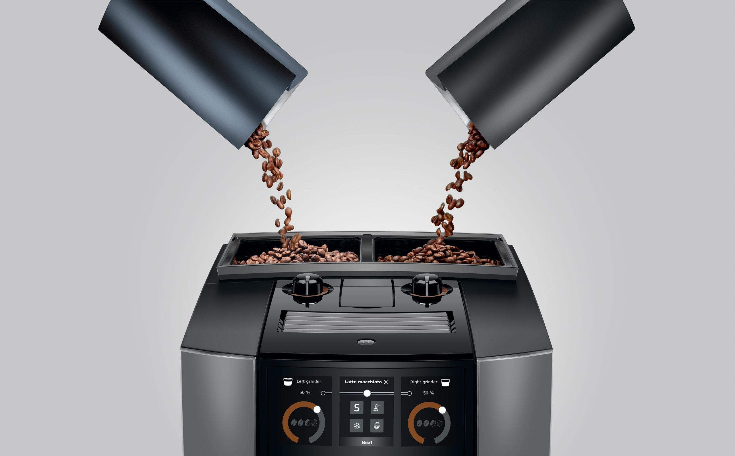 Kaffeebohnen fallen aus zwei Rohren in einen Kaffeevollautomaten.