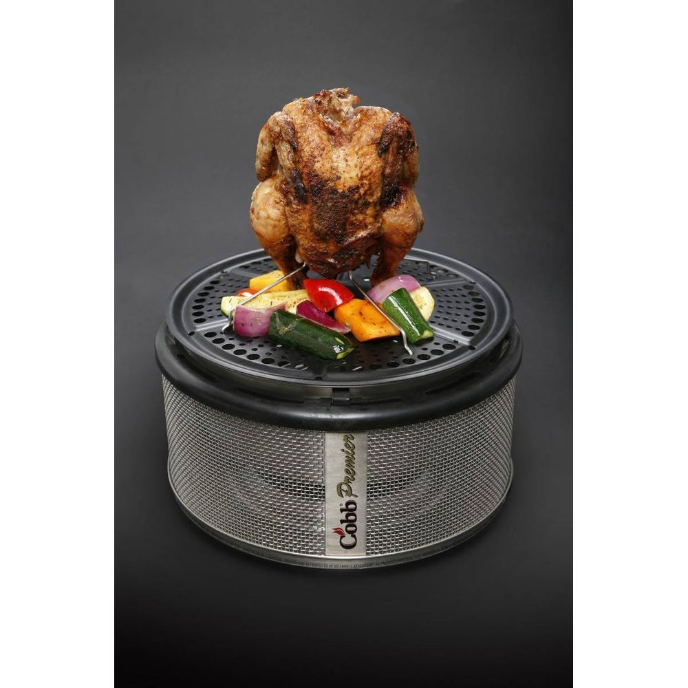 Un pollo arrosto siede su una griglia Cobb Premier con verdure colorate.