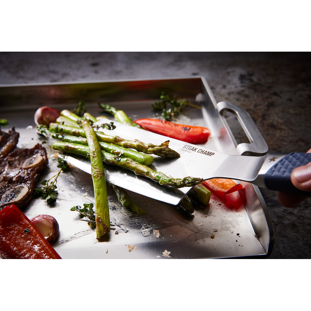 Carne, asparagi, peperoni e aglio su un vassoio di metallo con pinze da griglia.