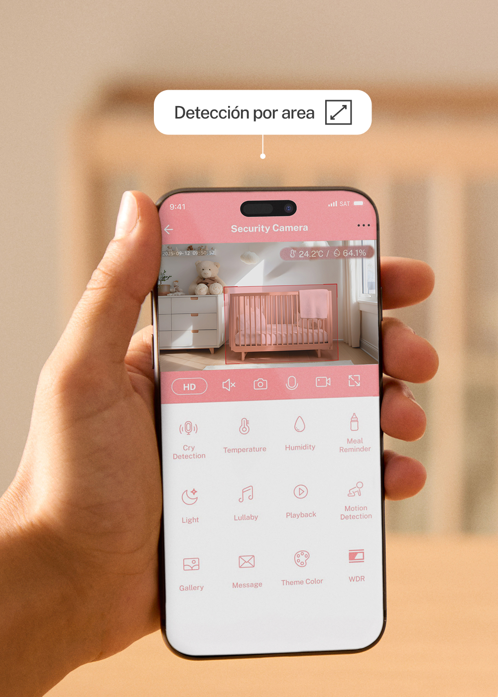 Una mano sostiene un smartphone que muestra una aplicación de cámara para bebés. Se ve una cuna rosa.