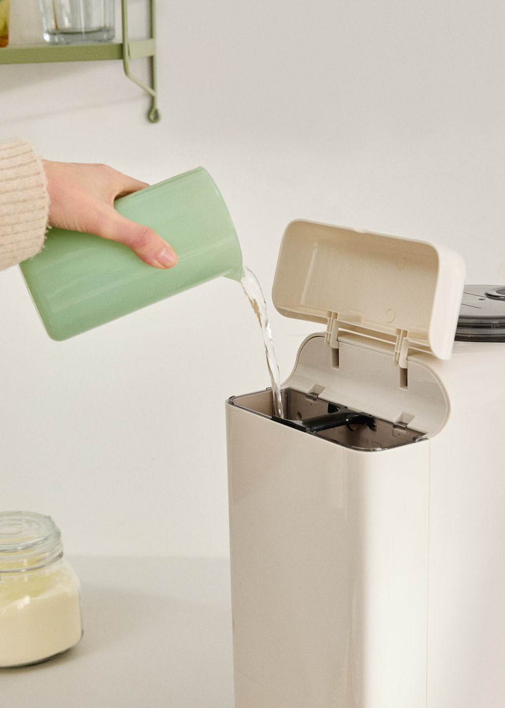 Una mano vierte agua de una taza verde a un electrodoméstico beige.
