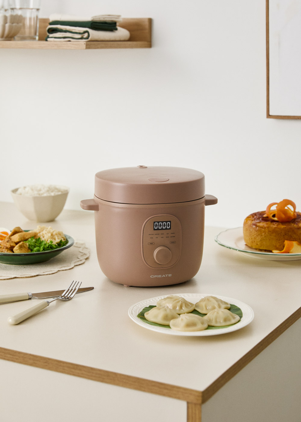 Una olla de cocción lenta marrón está sobre una mesa con comida, incluido un bol de arroz y un pastel.