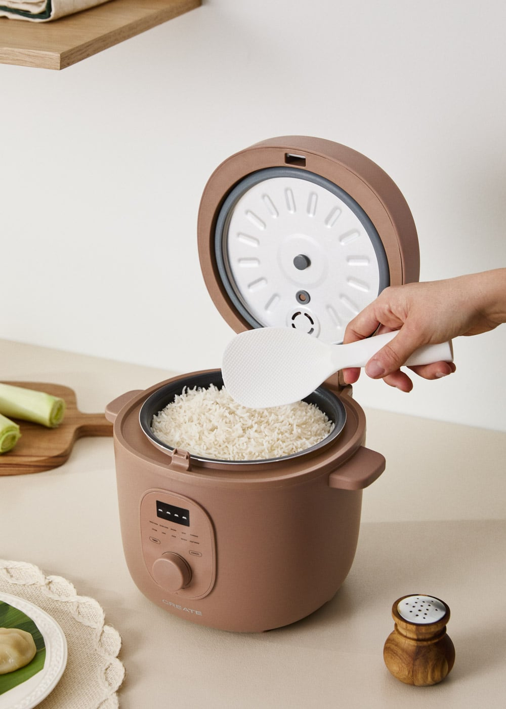 Una mano usa una pala de arroz blanca para servir arroz blanco esponjoso de una arrocera marrón.