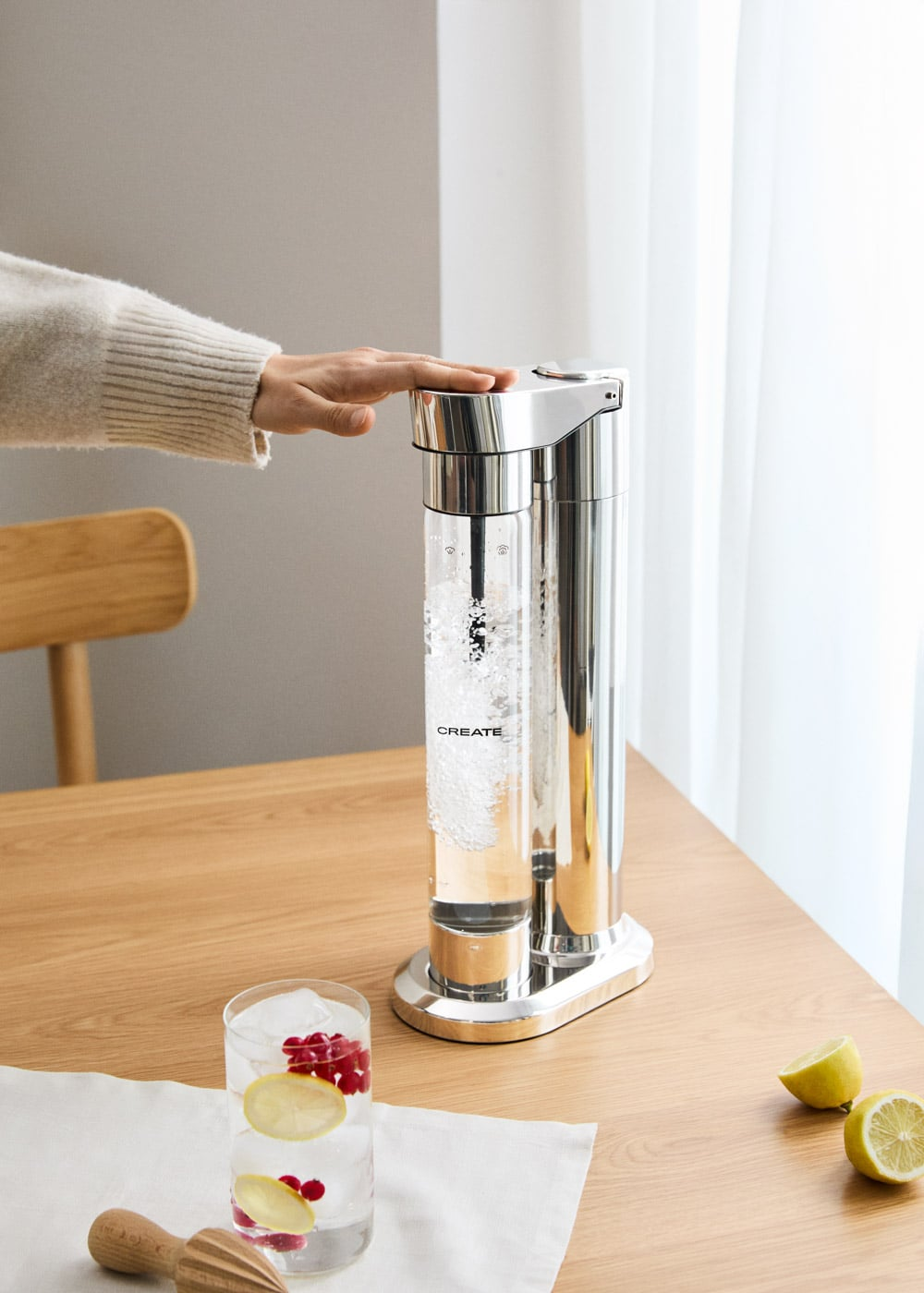 Una mano presiona una máquina de agua con gas en una mesa de madera.