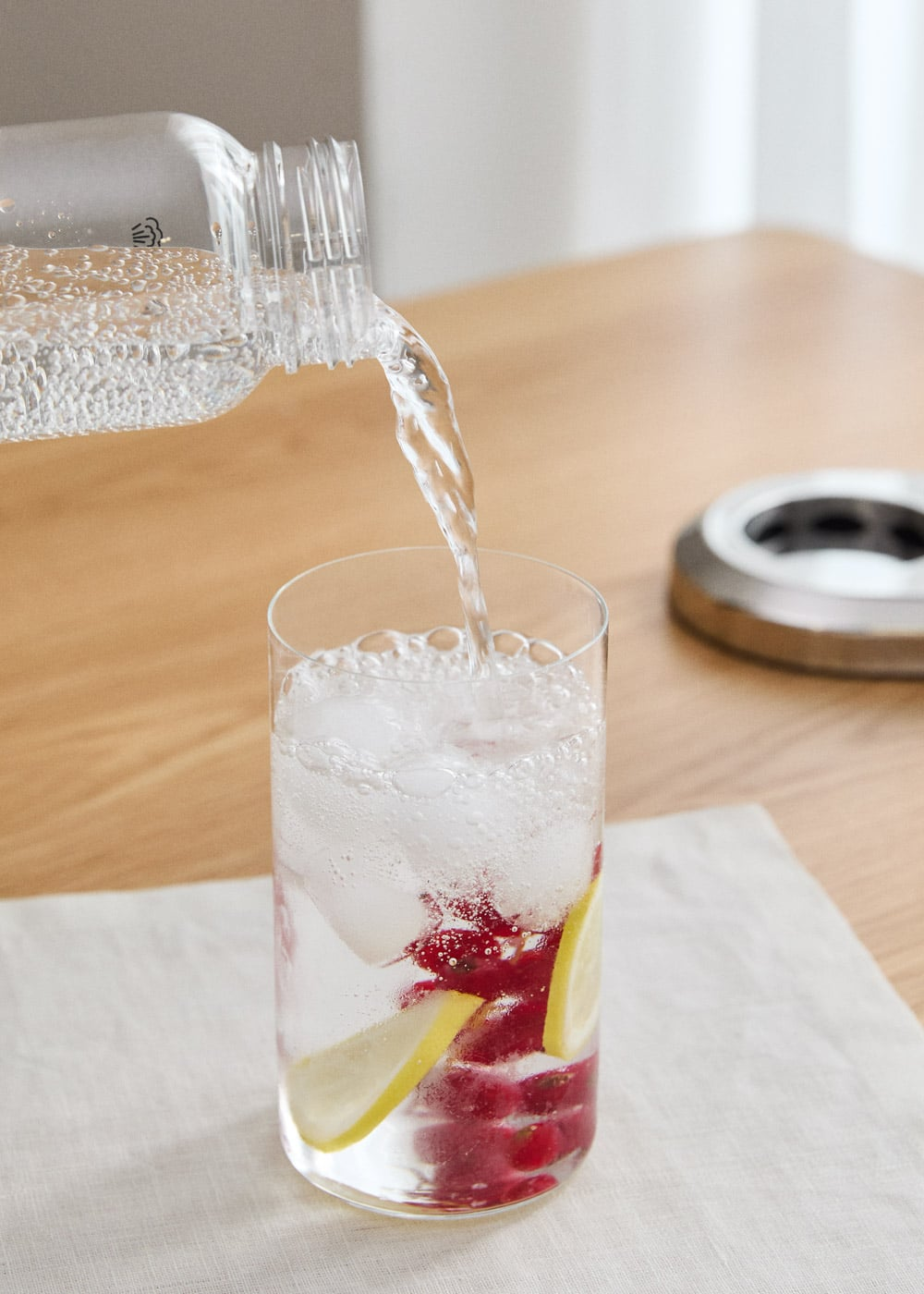 Se vierte agua con gas en un vaso con hielo, bayas y rodajas de limón.