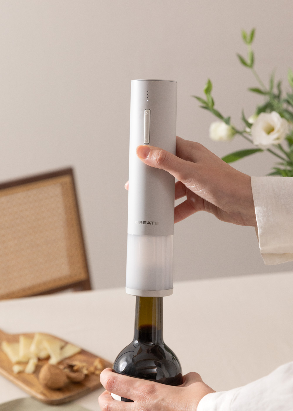 Una mano usa un abridor de botellas eléctrico blanco en una botella de vino.