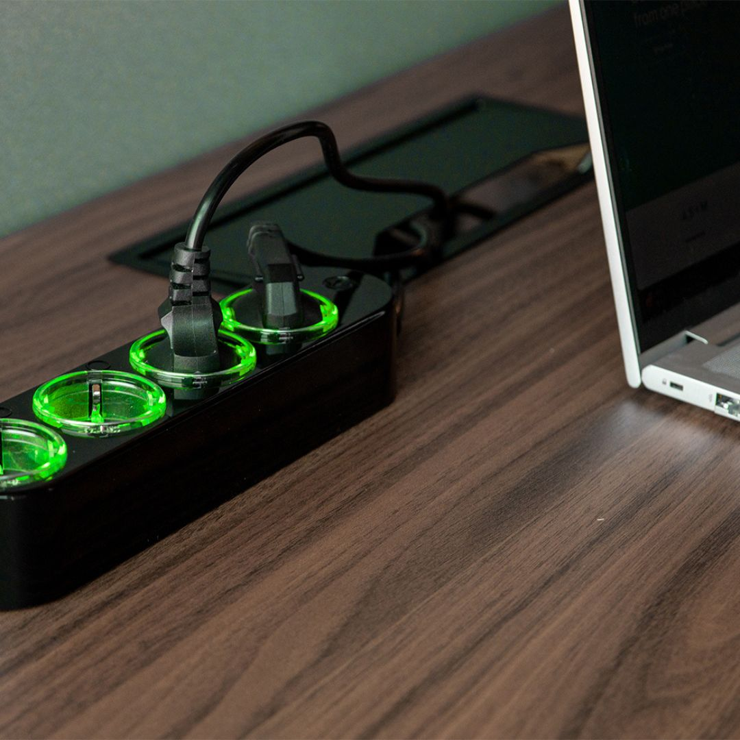 Multipresa nera con luci verdi e un laptop su una scrivania di legno.