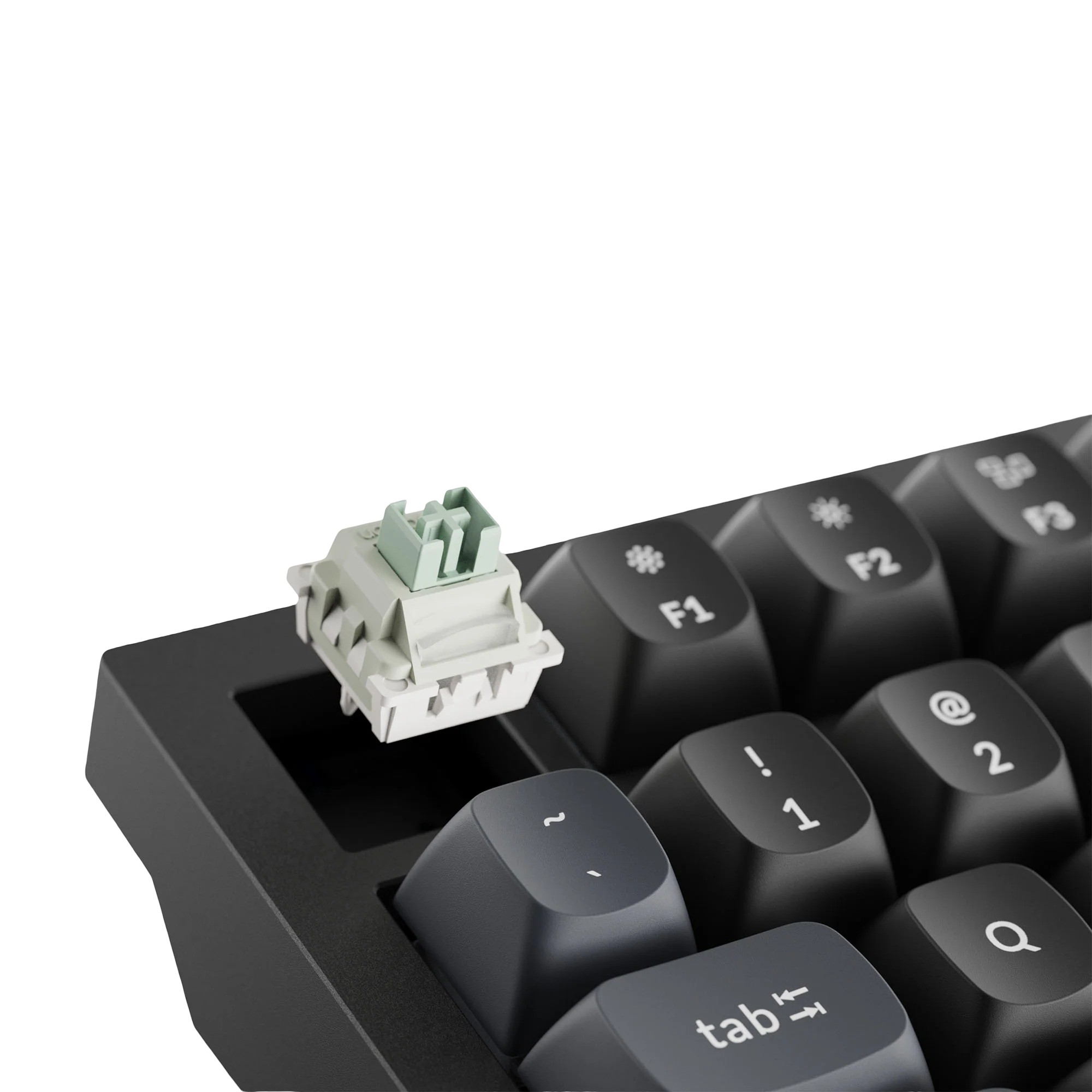 Szary mechaniczny przełącznik klawiatury z zieloną górną częścią na czarnej klawiaturze.