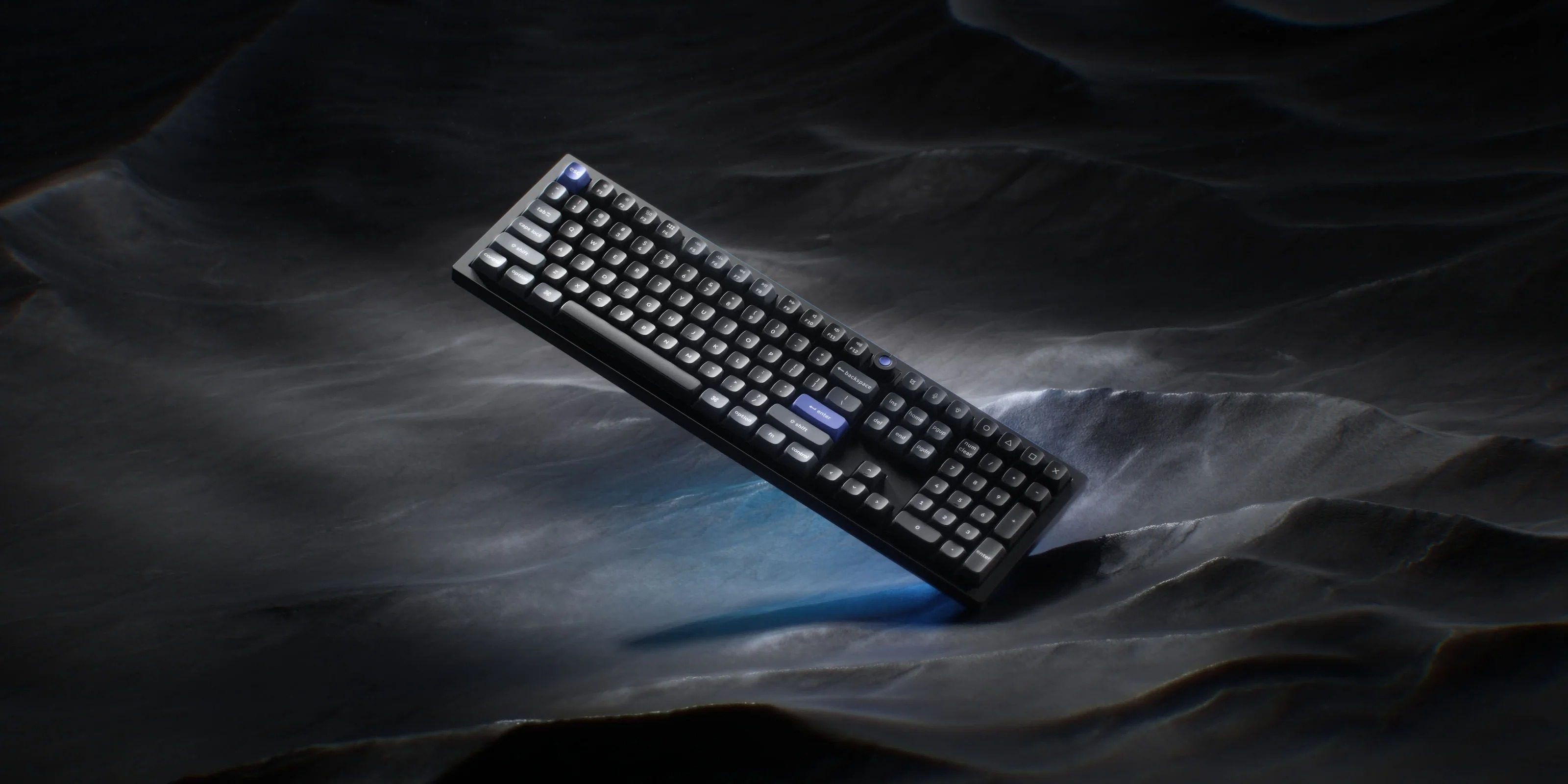 Czarna klawiatura spoczywa na ciemnej, falistej powierzchni z niebieskim światłem.