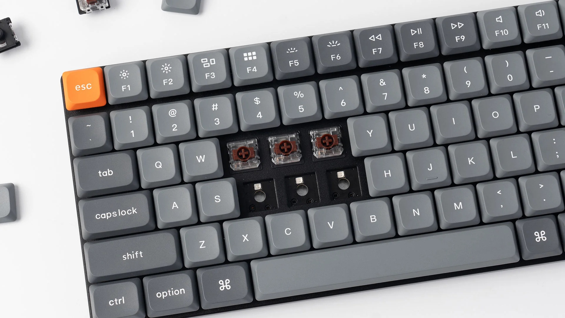 Szara klawiatura mechaniczna z pomarańczowym klawiszem ESC. Widoczne trzy przełączniki.