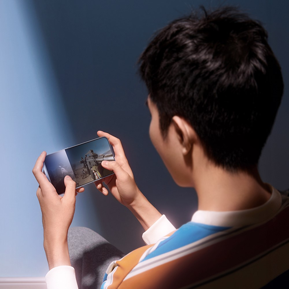 Un jeune joue à un jeu vidéo sur son téléphone, avec un mur bleu derrière.