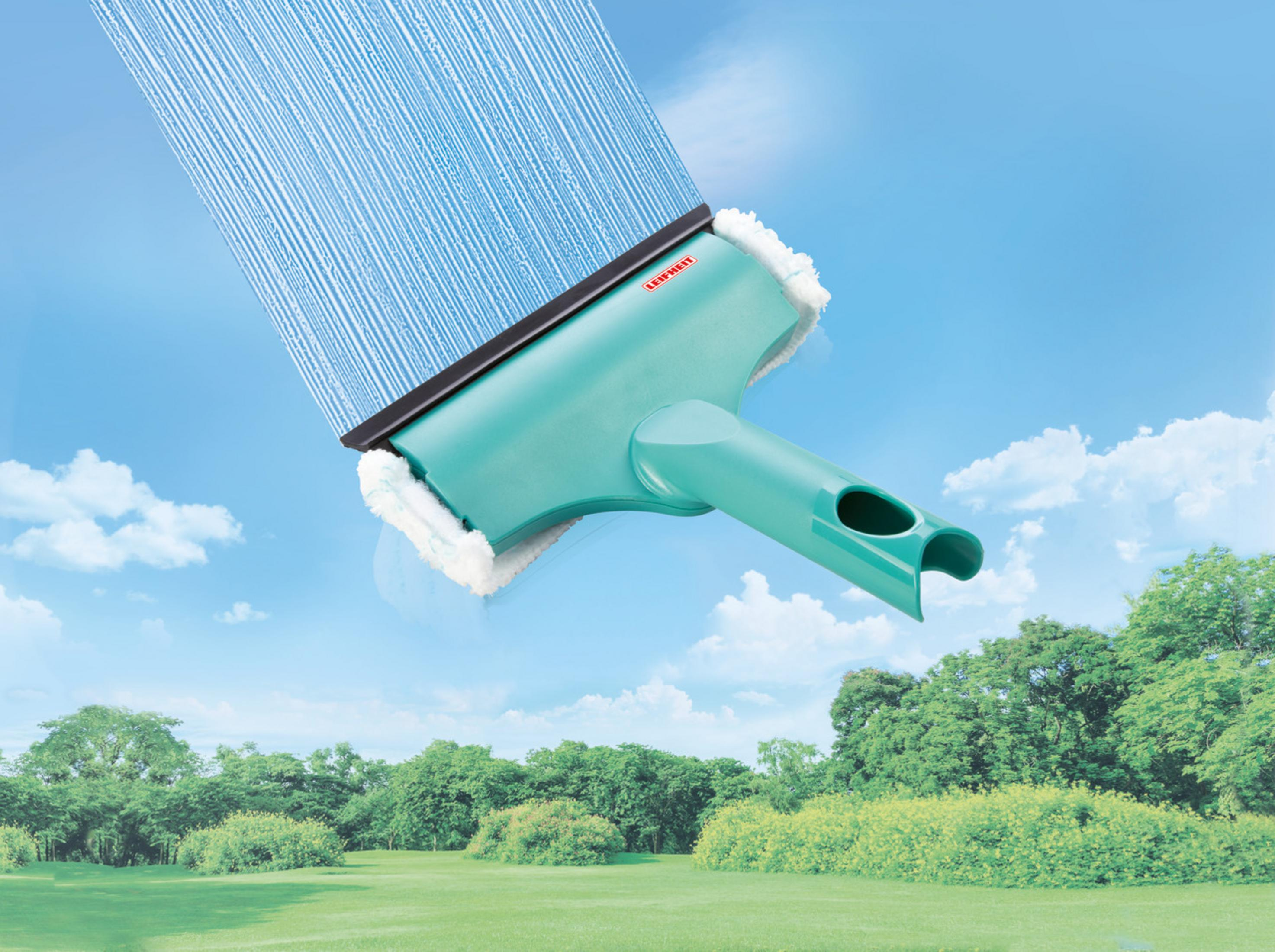 Ein grüner Fensterwischer mit blauem Schaumstoff vor blauem Himmel und grüner Landschaft.