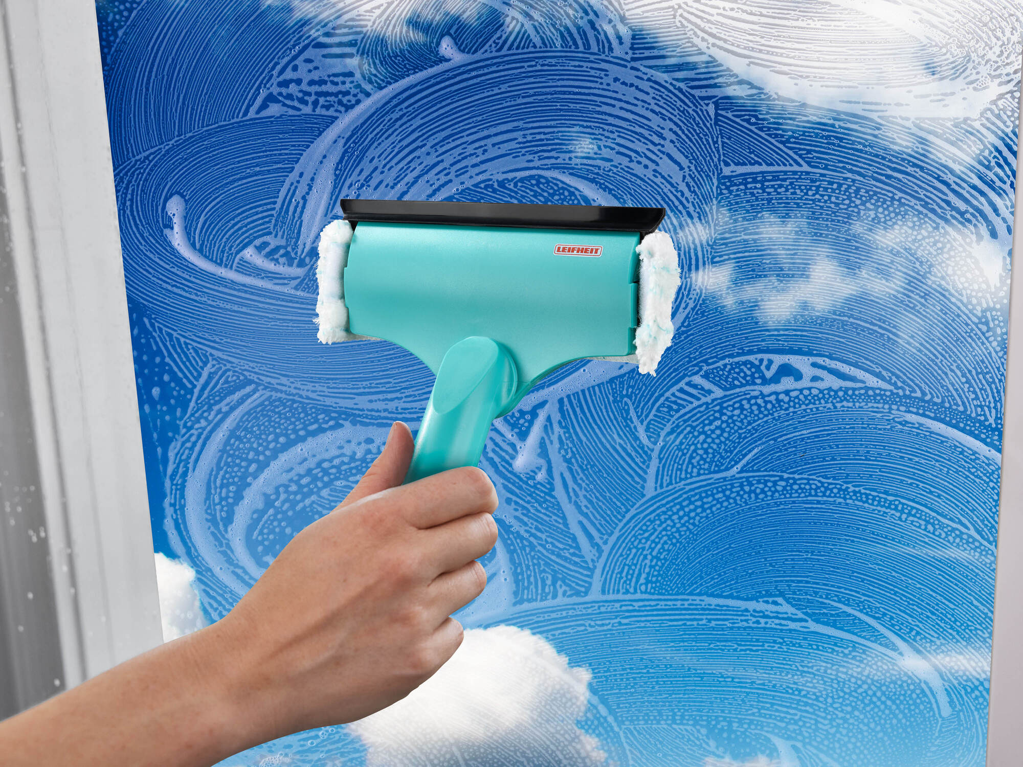 Eine Hand hält einen türkisfarbenen Fensterreiniger mit Seifenschaum auf einem blauen Fenster.