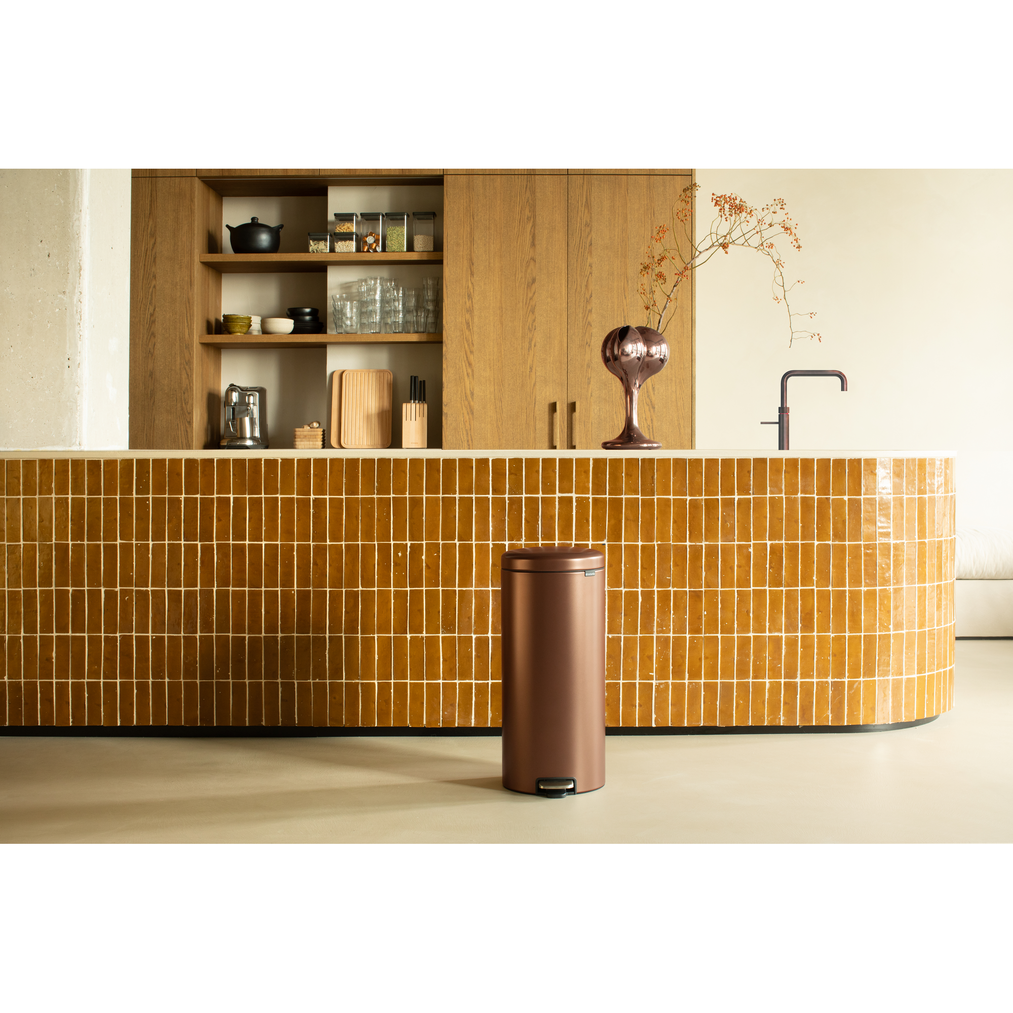 A copper trash can stands before a kitchen counter with ochre tiles.