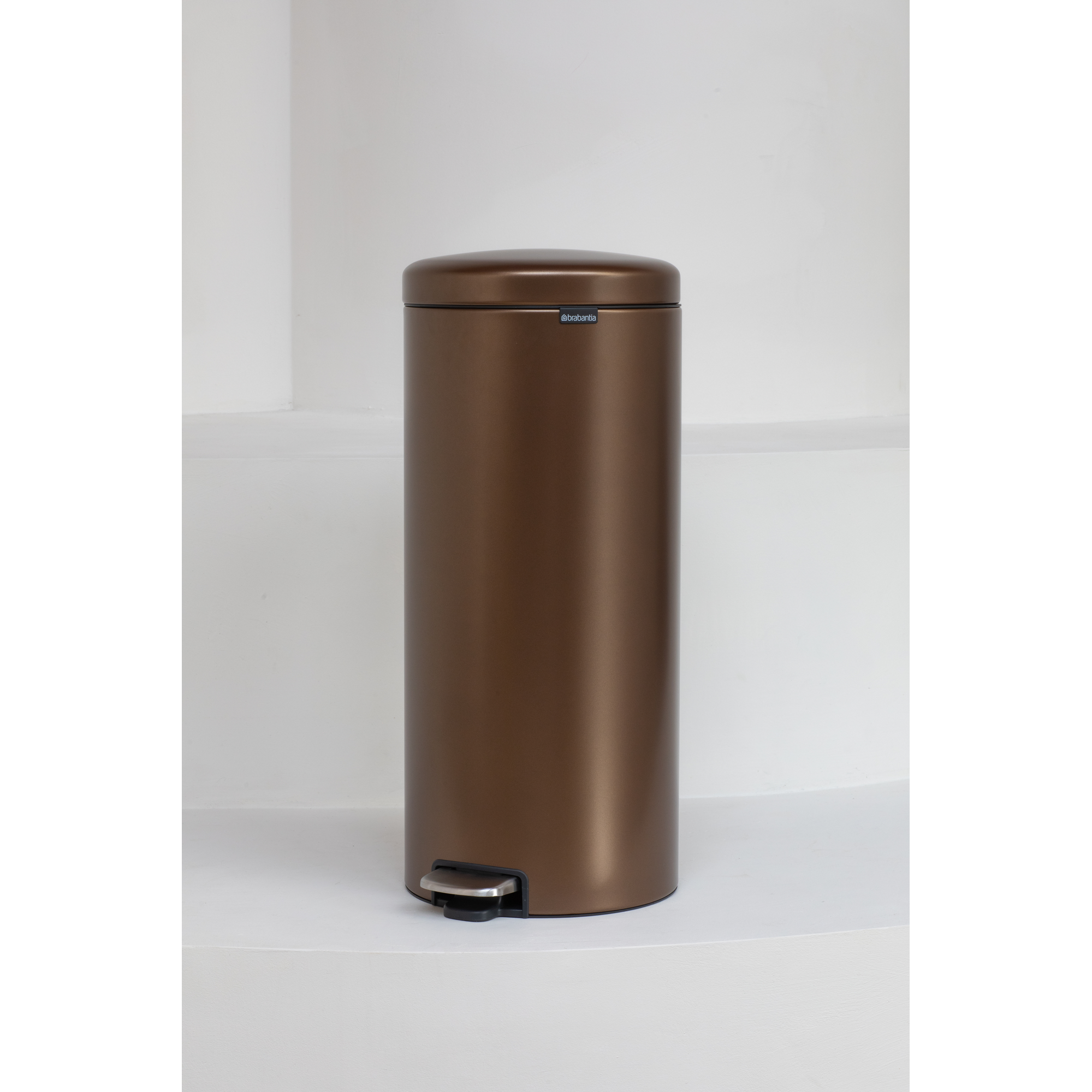 A bronze-colored step trash can stands on a white step.