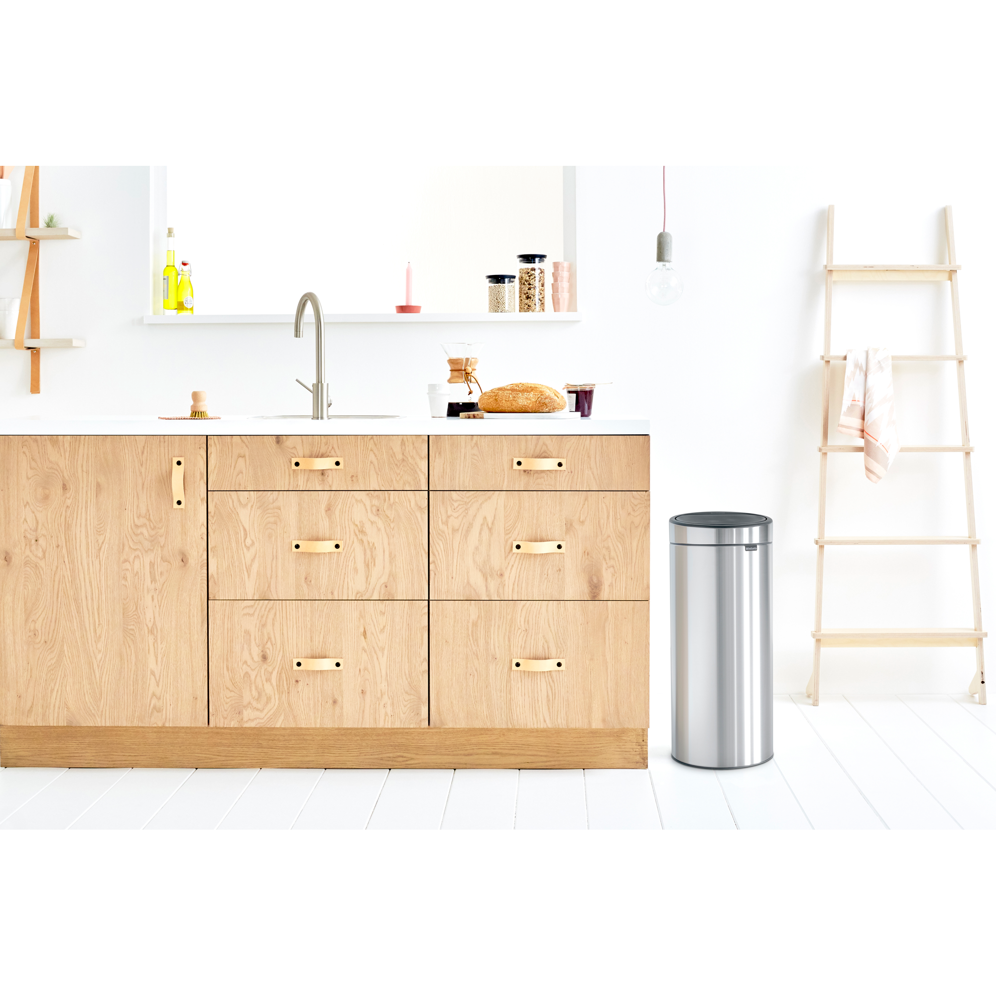 Modern kitchen with wood cabinets, sink, trash can and ladder.