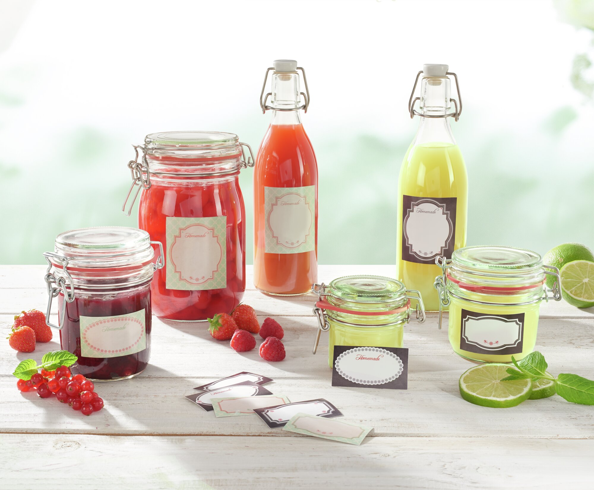 Gläser mit Fruchtsaft und Marmelade, Beeren, Limetten und Minze auf Holztisch.