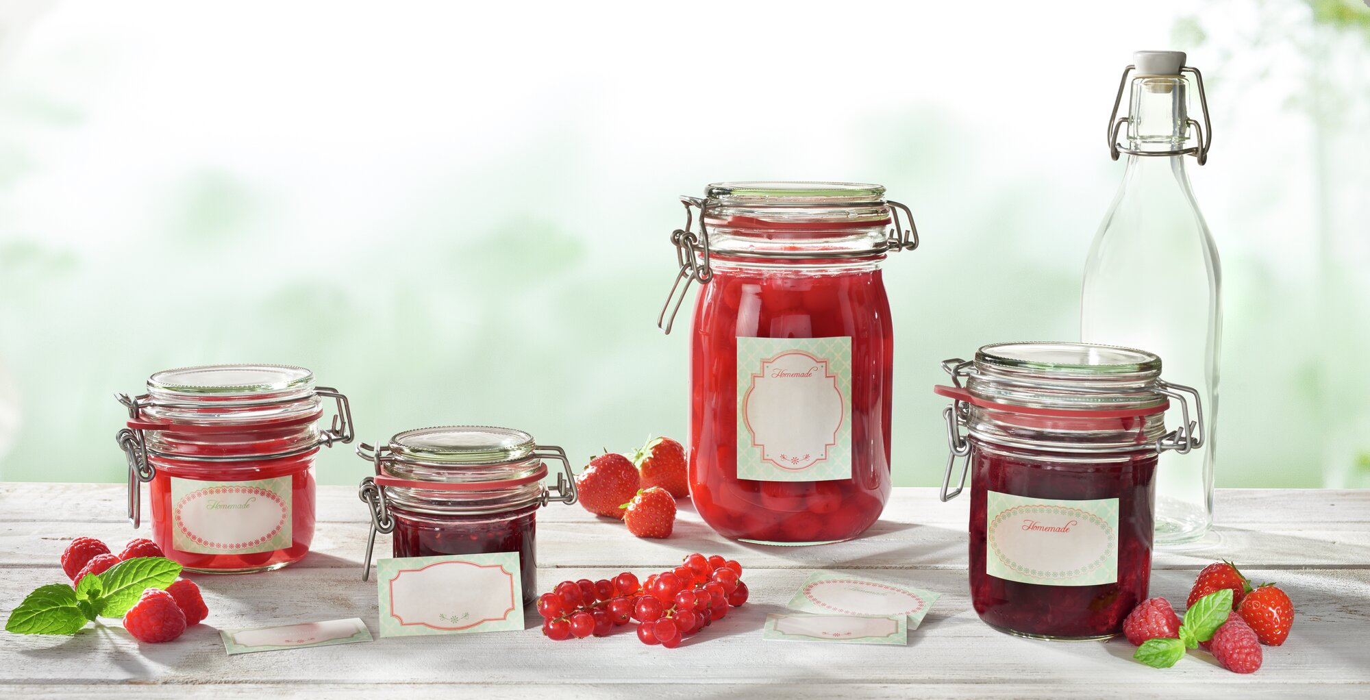 Drei Einmachgläser mit roter Marmelade oder Kirschen, Beeren und eine Glasflasche.