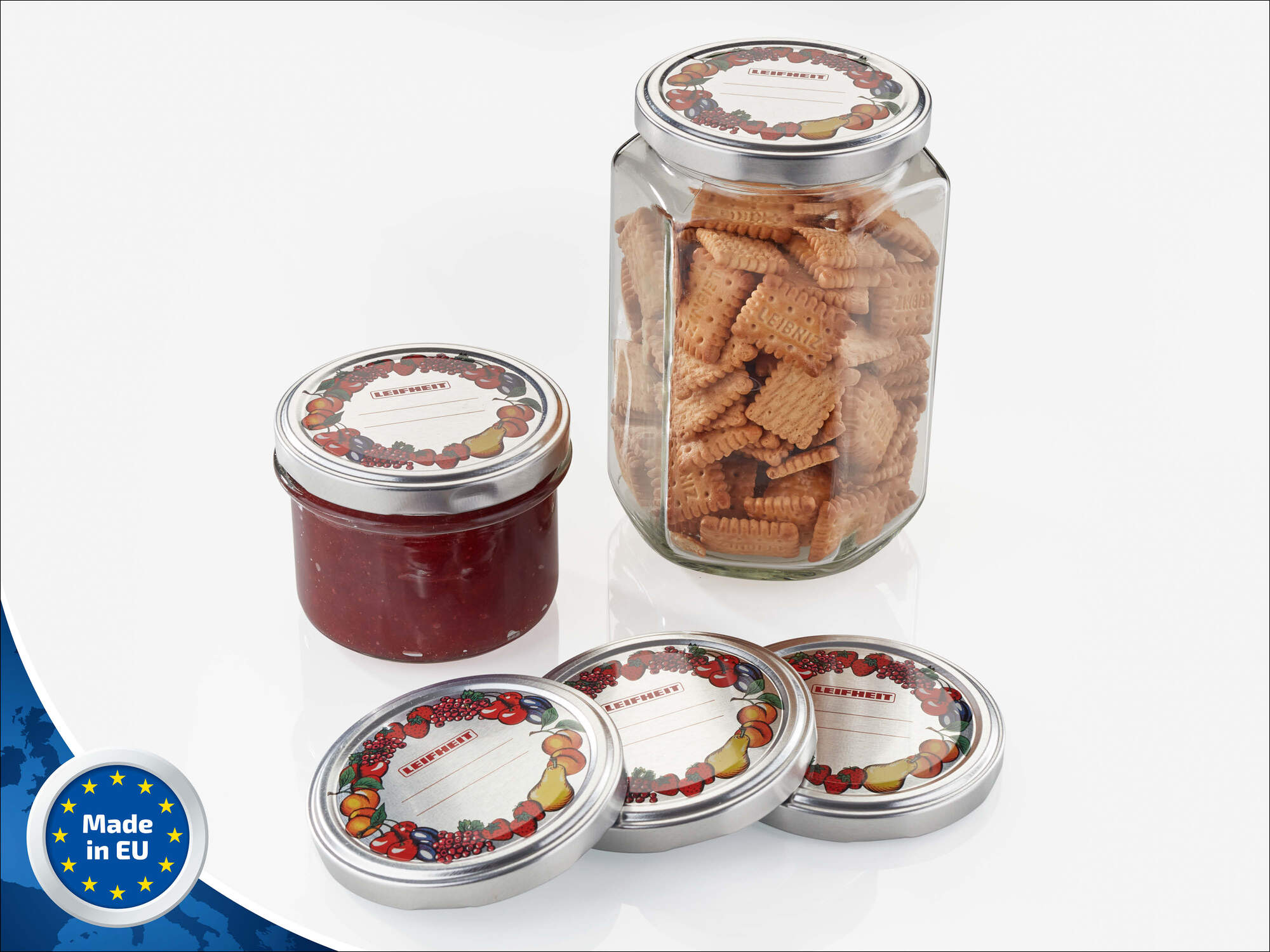 Ein Glas Kekse und ein Glas Marmelade mit drei Deckeln mit Fruchtmuster.