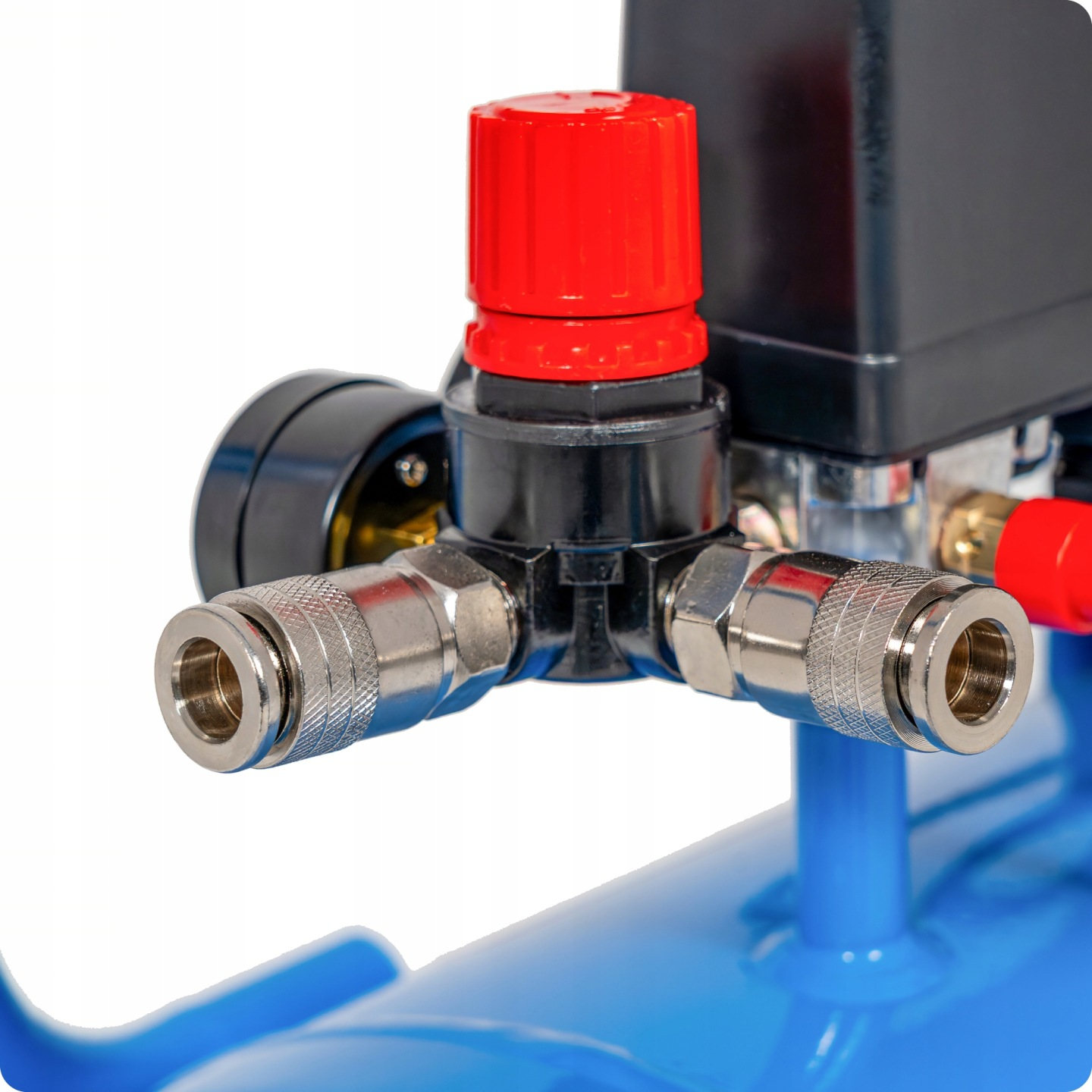 Zbliżenie regulatora ciśnienia z czerwonym pokrętłem, manometrem i srebrnymi złączami.