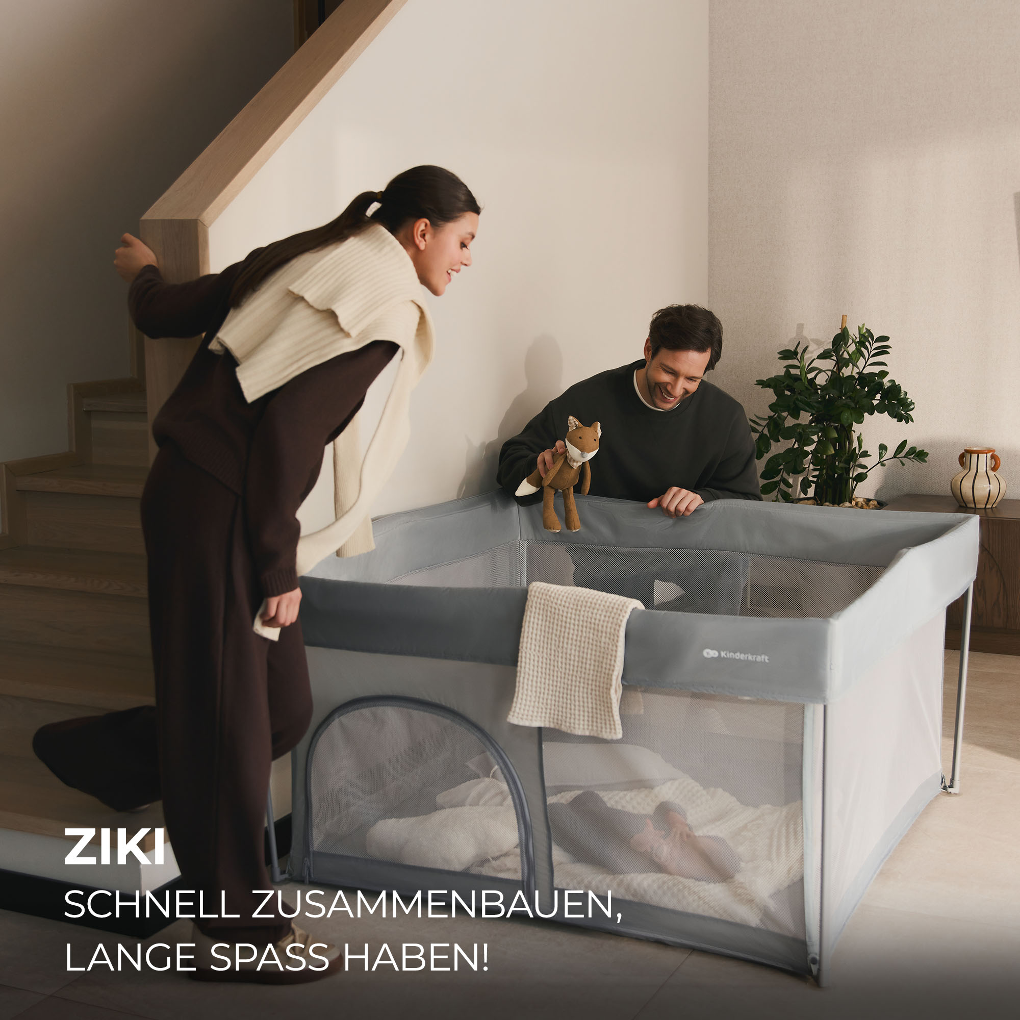 Ein Mann und eine Frau stehen neben einem grauen Laufstall mit einem Fuchs-Stofftier.