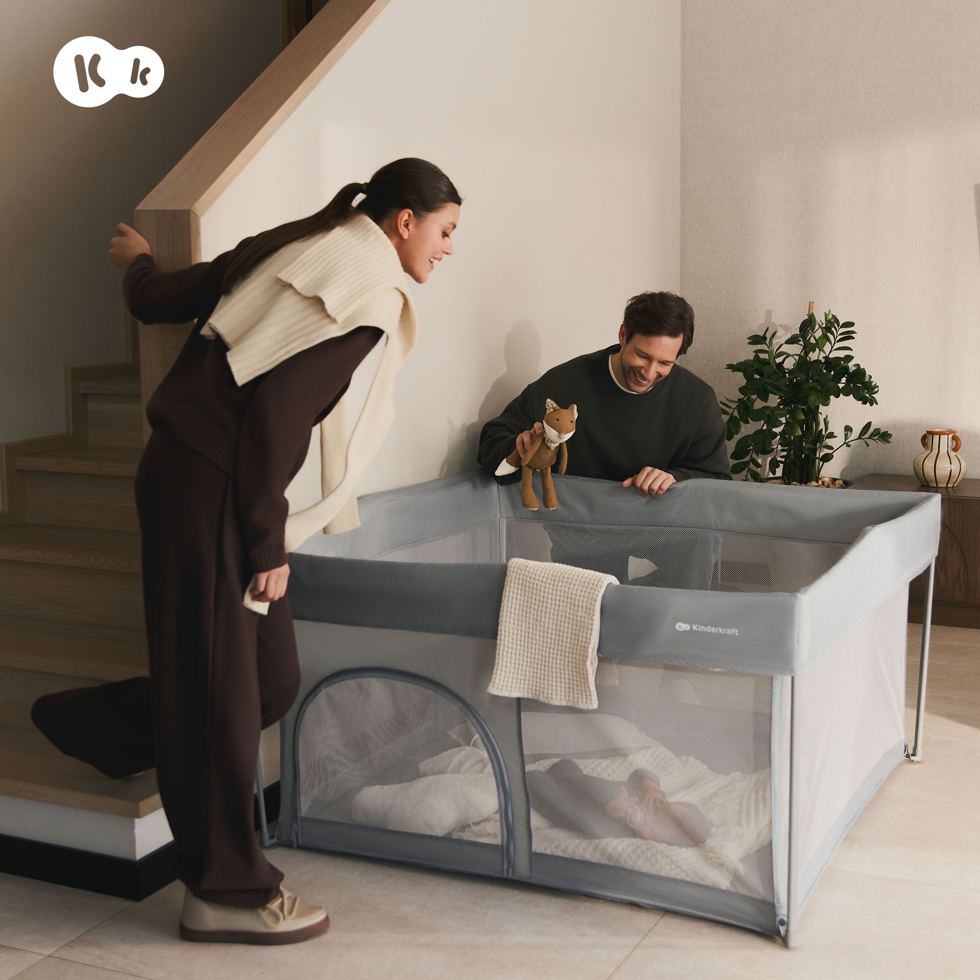 Ein Mann hält ein Fuchs-Stofftier über ein Reisebett, eine Frau schaut zu.