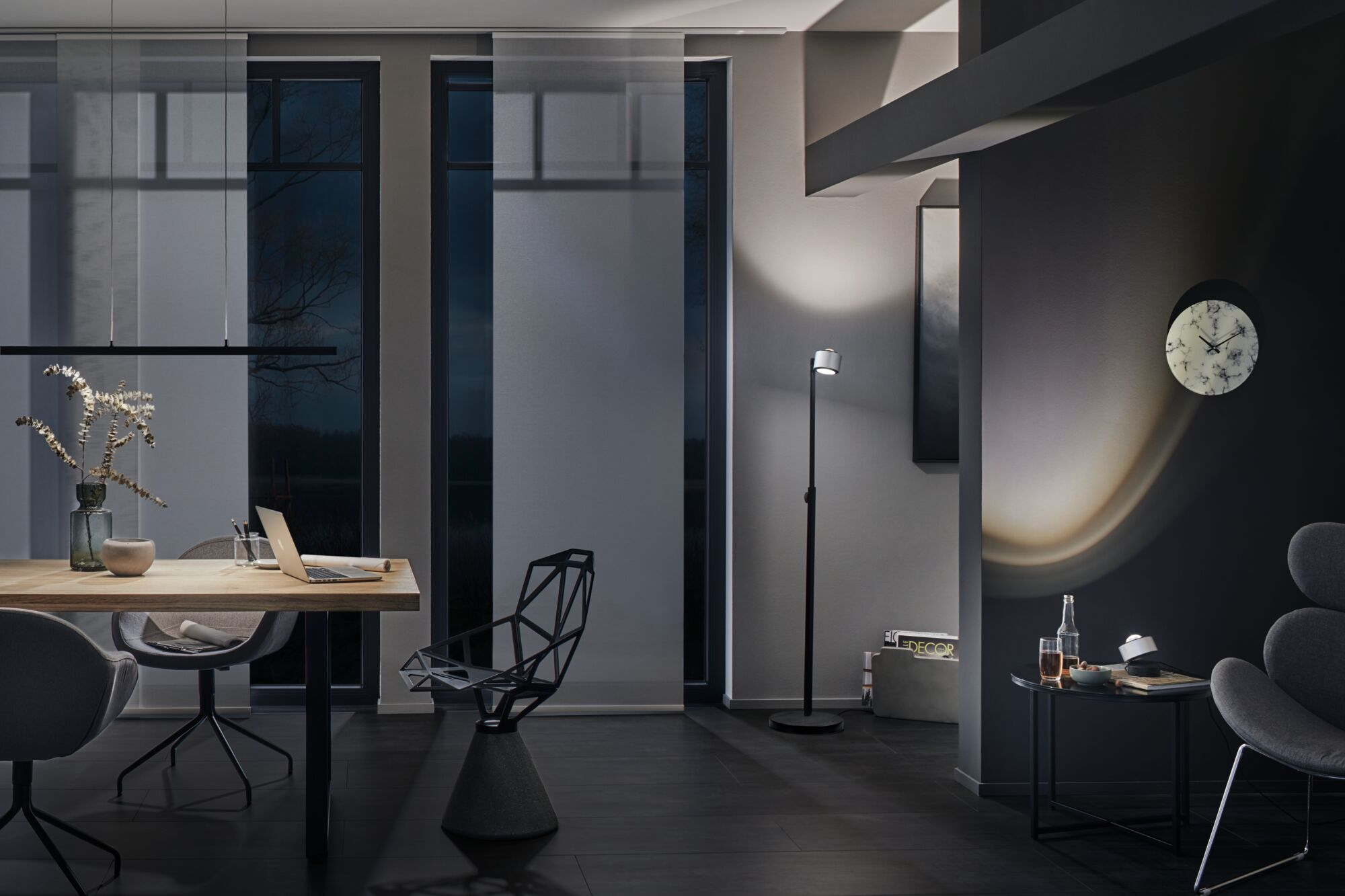 Intérieur moderne avec table à manger, ordinateur portable, chaise, lampadaire et horloge.