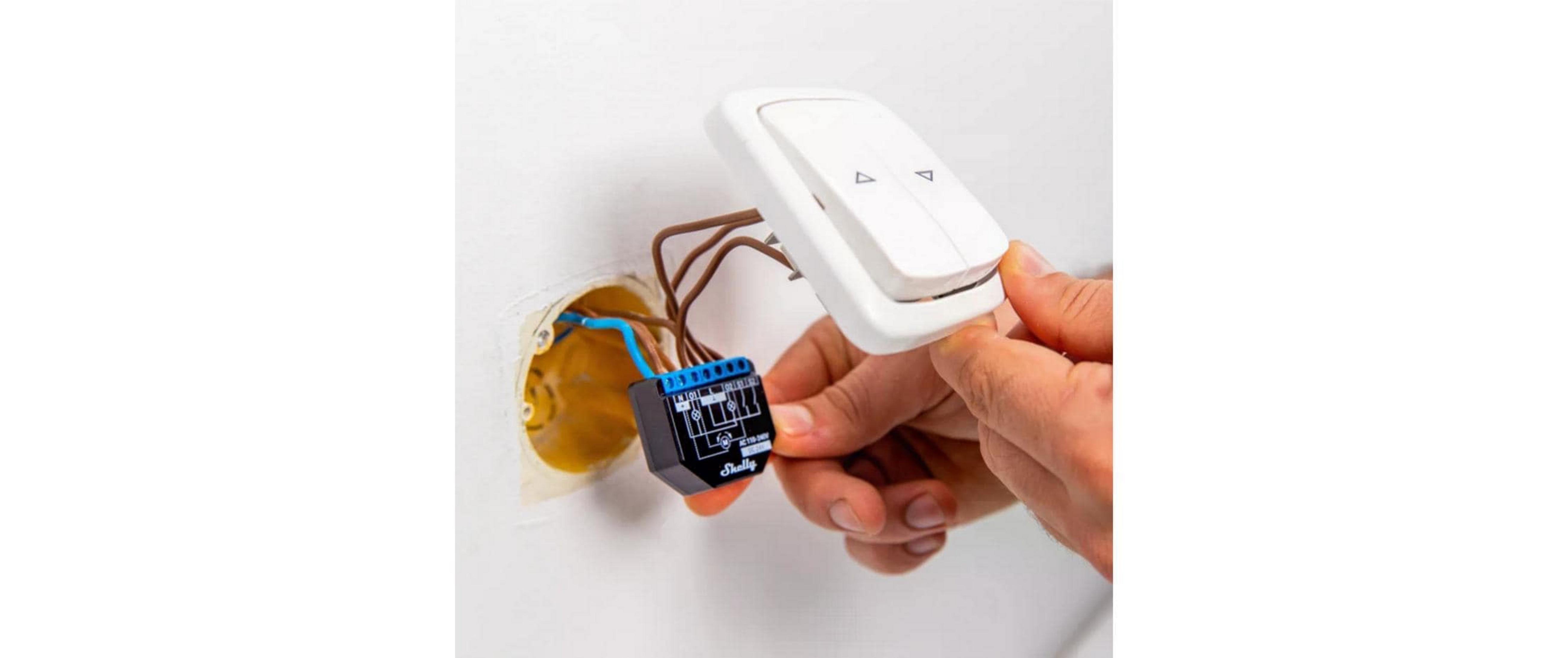 Mani cablano un interruttore della luce bianco e un dispositivo smart home nero in una presa a muro.