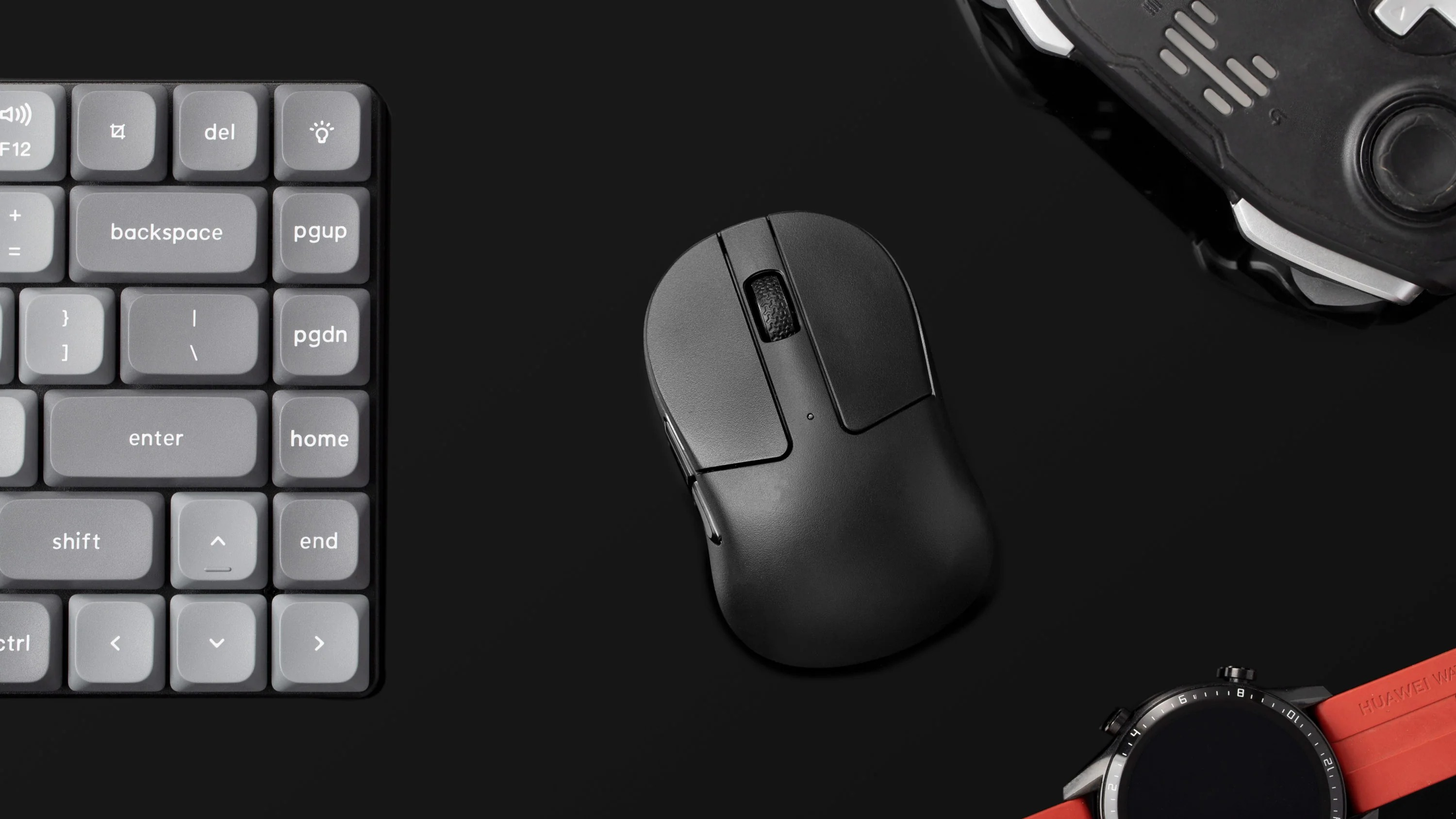 Szara klawiatura, czarna mysz, kontroler do gier i smartwatch na czarnym tle.