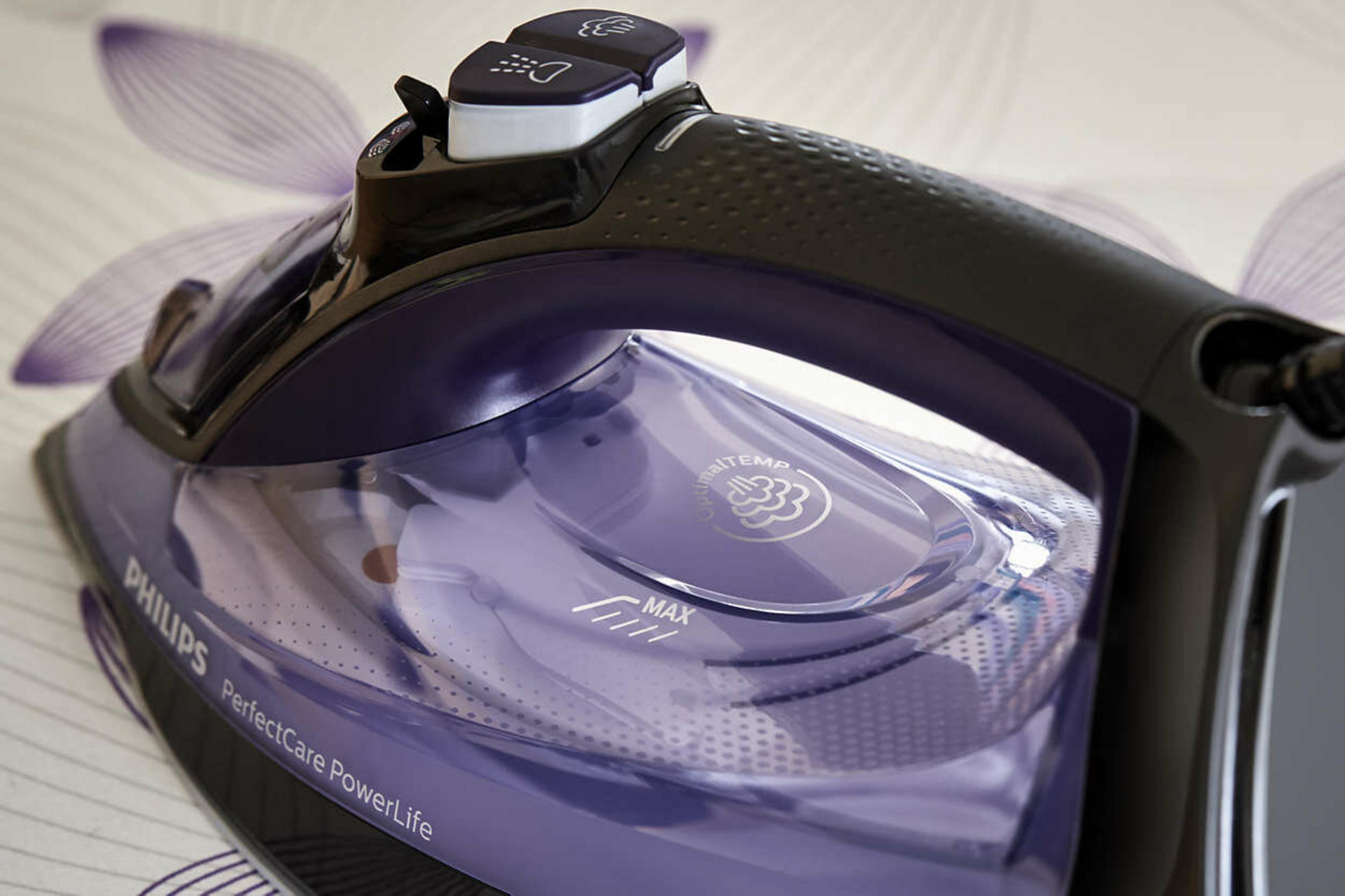 Ein violetter Philips Dampfbügeleisen mit schwarzem Griff liegt auf gemustertem Stoff.
