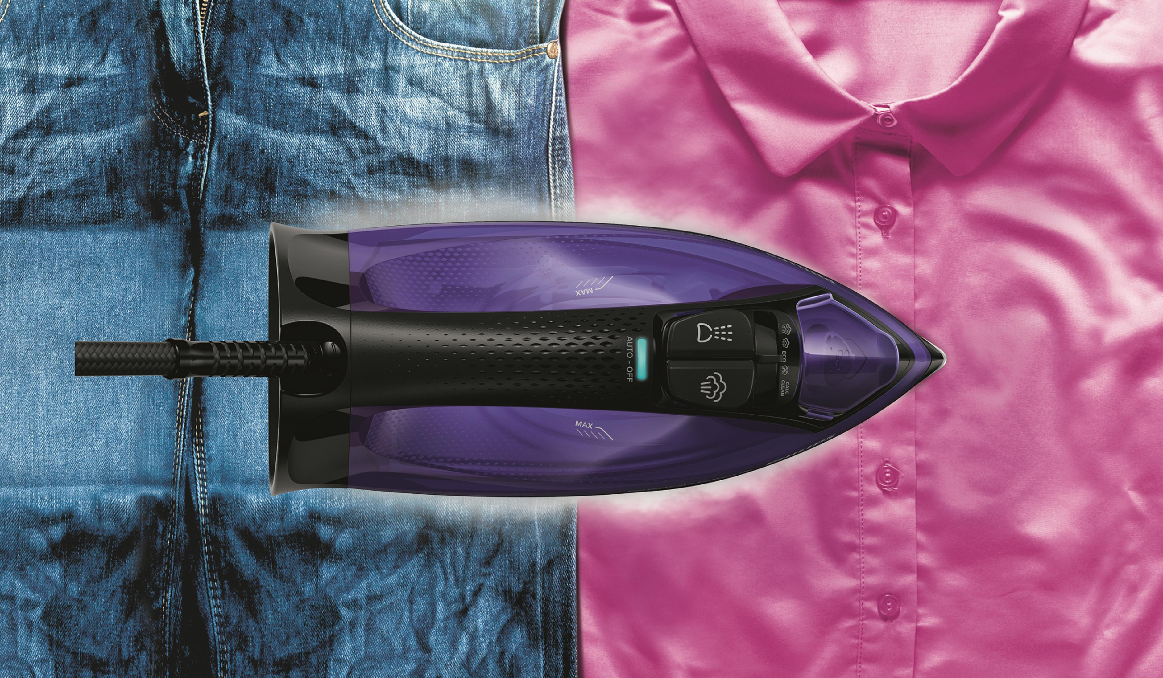 Ein Bügeleisen glättet ein pinkes Hemd und blaue Jeans mit Dampf.